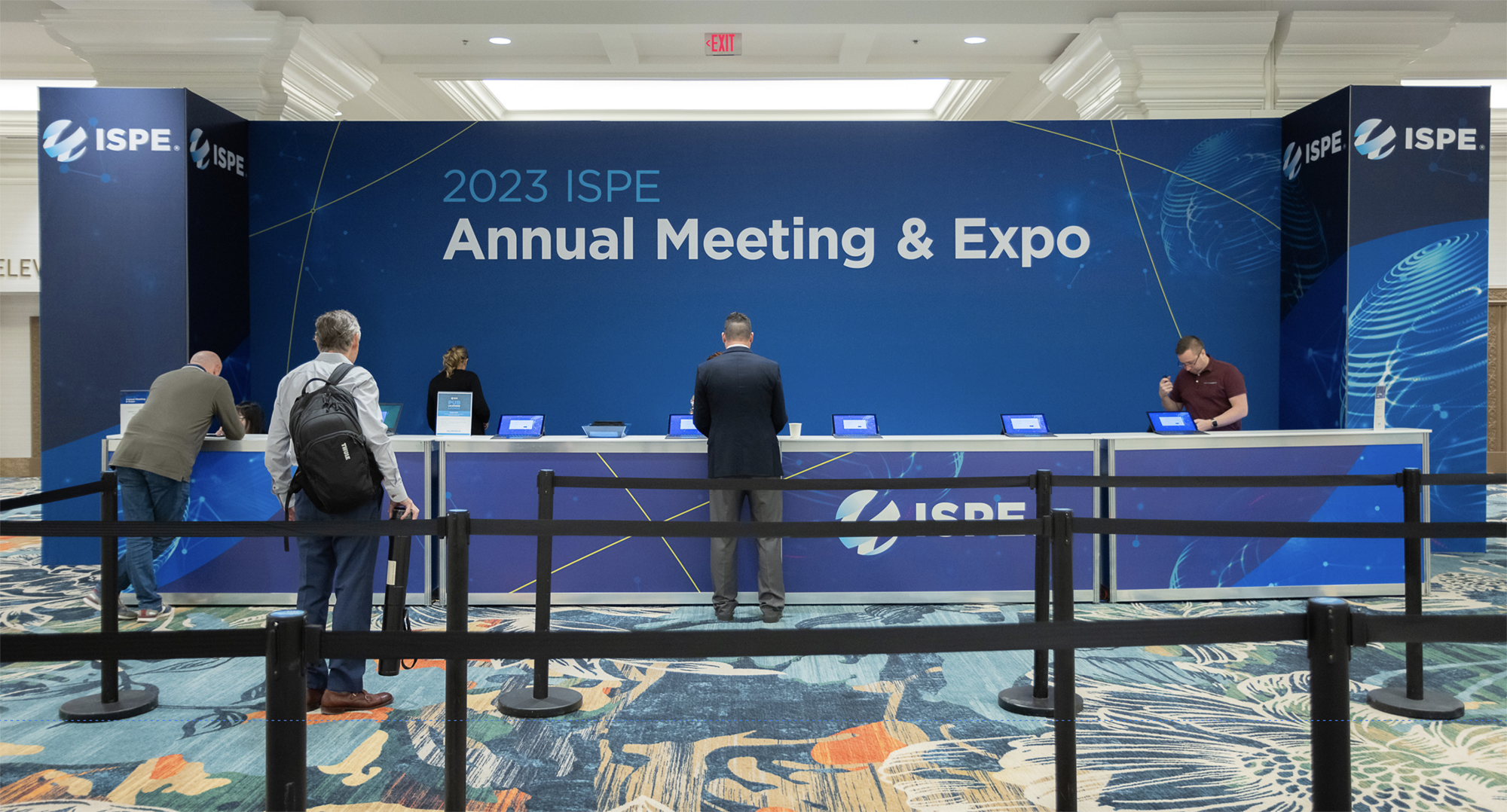 Registration area for the 2023 ISPE Annual Meeting & Expo. A long counter with blue ISPE branding and signage reads “Annual Meeting & Expo” as attendees check in.